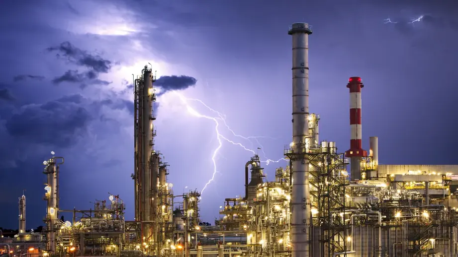 Refinaria em operação à noite, com relâmpago ao fundo